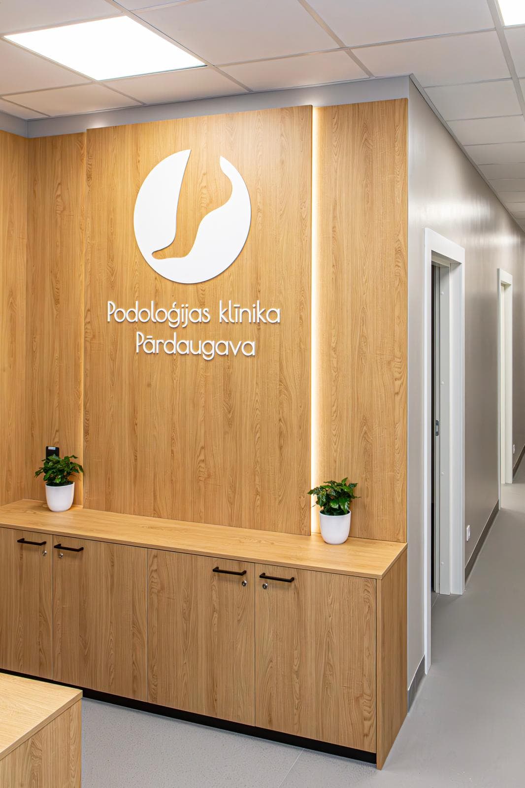 Podoloģijas Klīnikas Pārdaugava reģistratūra ar klīnikas logo uz koka sienas